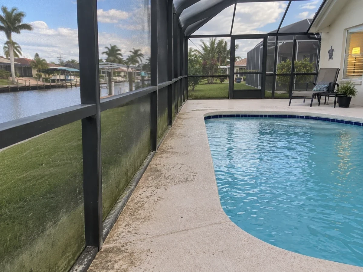 A screened pool enclosure with fine algae film along the bottom rail and tracked sand on the deck.