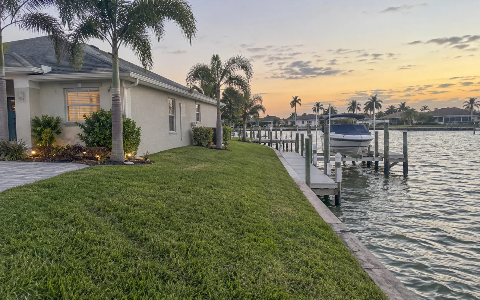 A canal-front Cape Coral home seen from the corner of its lot, showing the side and back corner of the house with the private dock and boat lift on the canal behind.