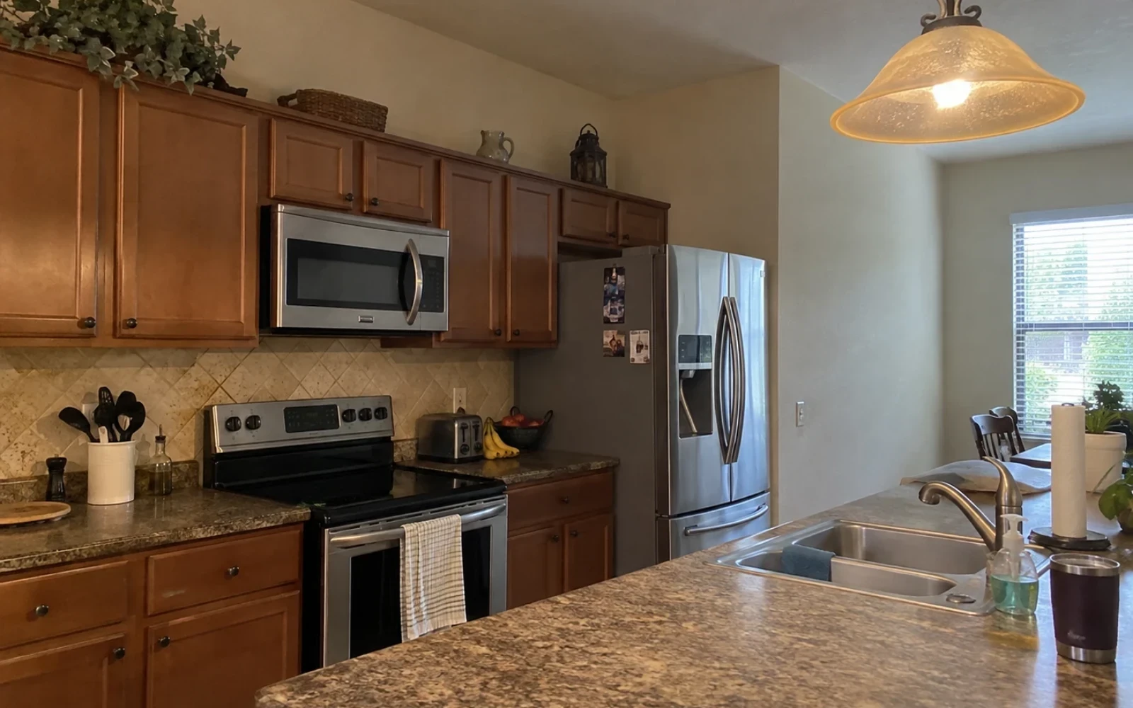 A lived-in kitchen with light grease film on a tile splashback and everyday clutter on the counter before a thorough clean.