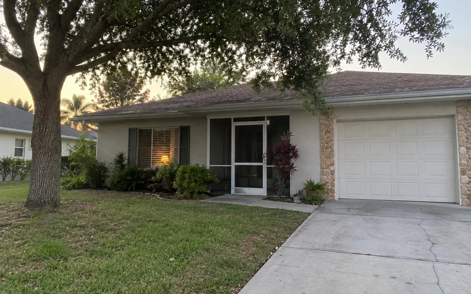 An older single-storey Fort Myers home with a mature tree and a screened front entry.