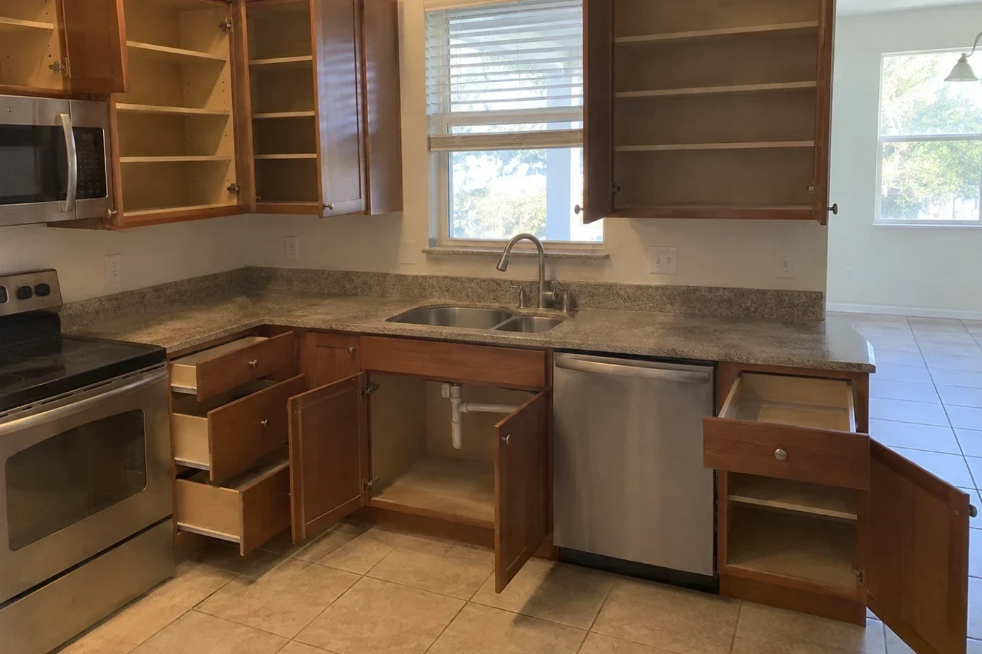 Open empty kitchen cabinets and drawers with visible dust and fine residue inside.
