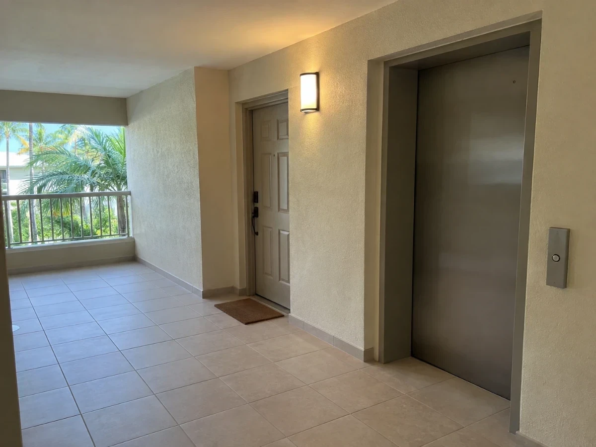 A clean condominium corridor with a tiled floor, an unbranded unit door, and an elevator door.