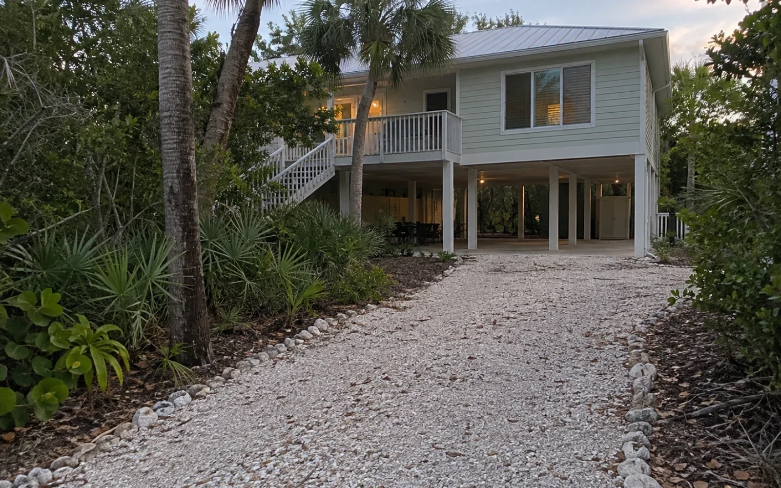 An elevated island home with native vegetation and a shell driveway.
